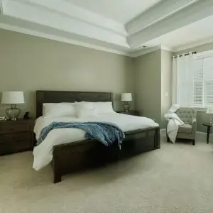 A cozy bedroom featuring a bed, dresser, and a window, with a plush carpet typical of Dubai interiors.